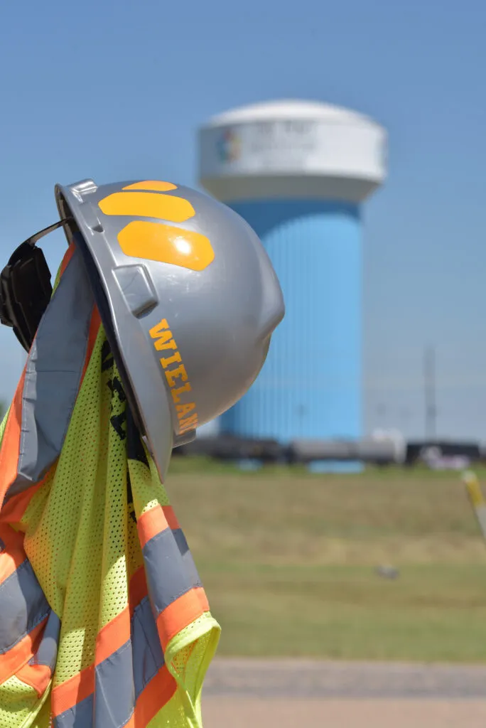 WIELAND branded hard hat and safety vest hang on a shovel.