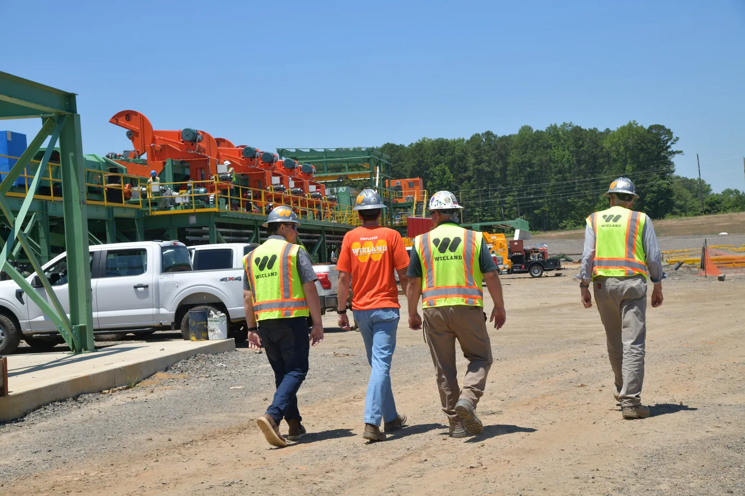 Employees in safety gear walk down a project site dirt road.