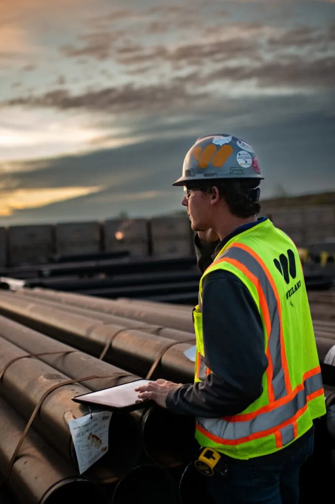 Team member talks on the phone, standing at a worksite with tablet in hand.