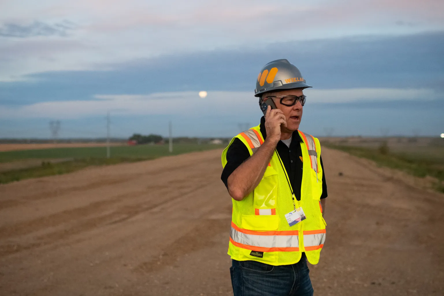 WIELAND team member in safety gear stands in a dirt lot while on a phone call