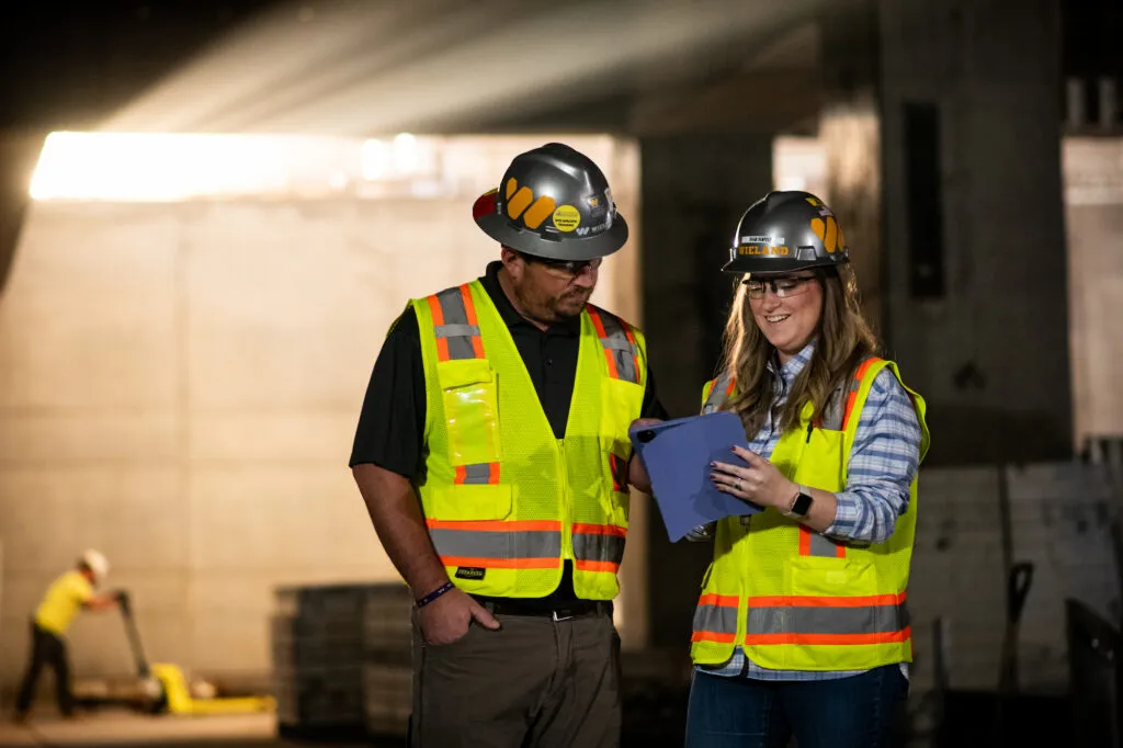 Two safety-gear wearing WIELAND team members discuss over documents.