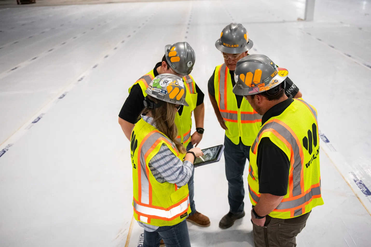 Safety gear-clad WIELAND team members discuss over tablet in a bright white work site.