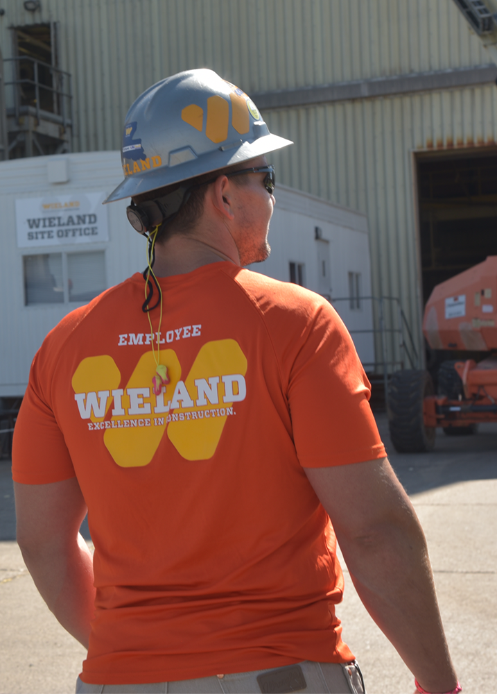 Employee in bright orange WIELAND-branded t-shirt and hard hat.