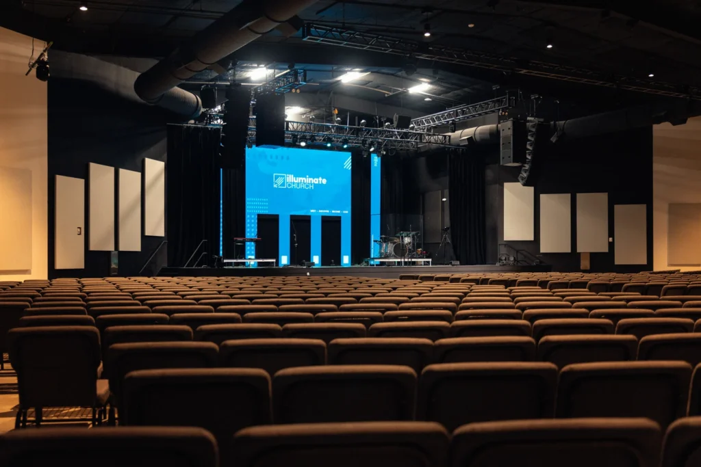Interior view of a spacious auditorium at Illuminate Church, Celebration, FL, with neatly arranged rows of chairs.