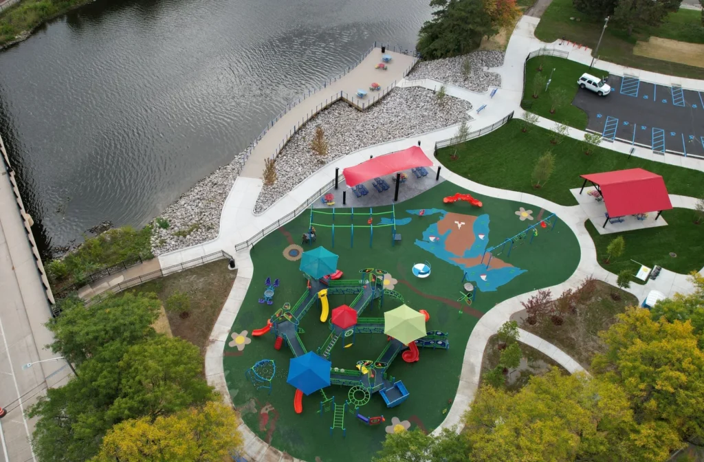 Overhead view of a Lansing, MI playground with colorful equipment and a flowing river adjacent to it.