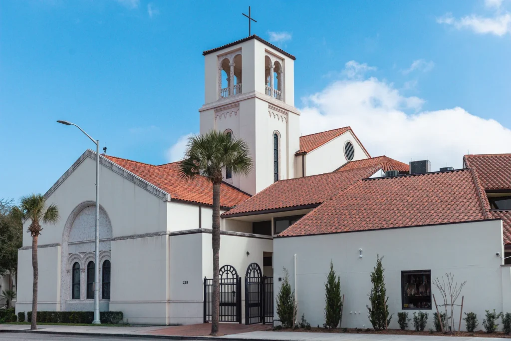 A view of St. James Catholic Church, a white building topped with a red roof, situated in Orlando, FL.