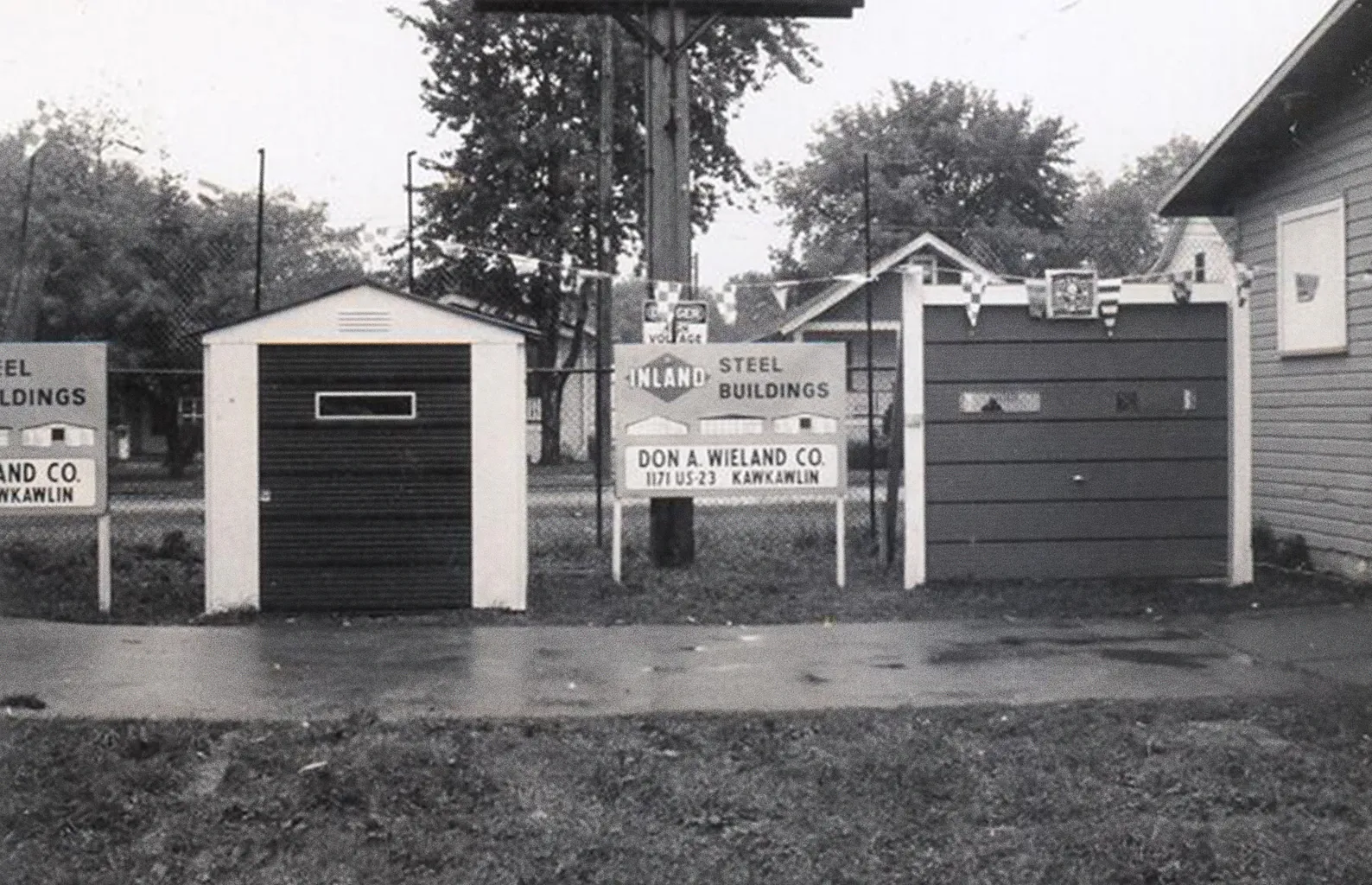 Two small sheds bracket a sign stating "Inland Steel Buildings, Don A. Wieland Co."