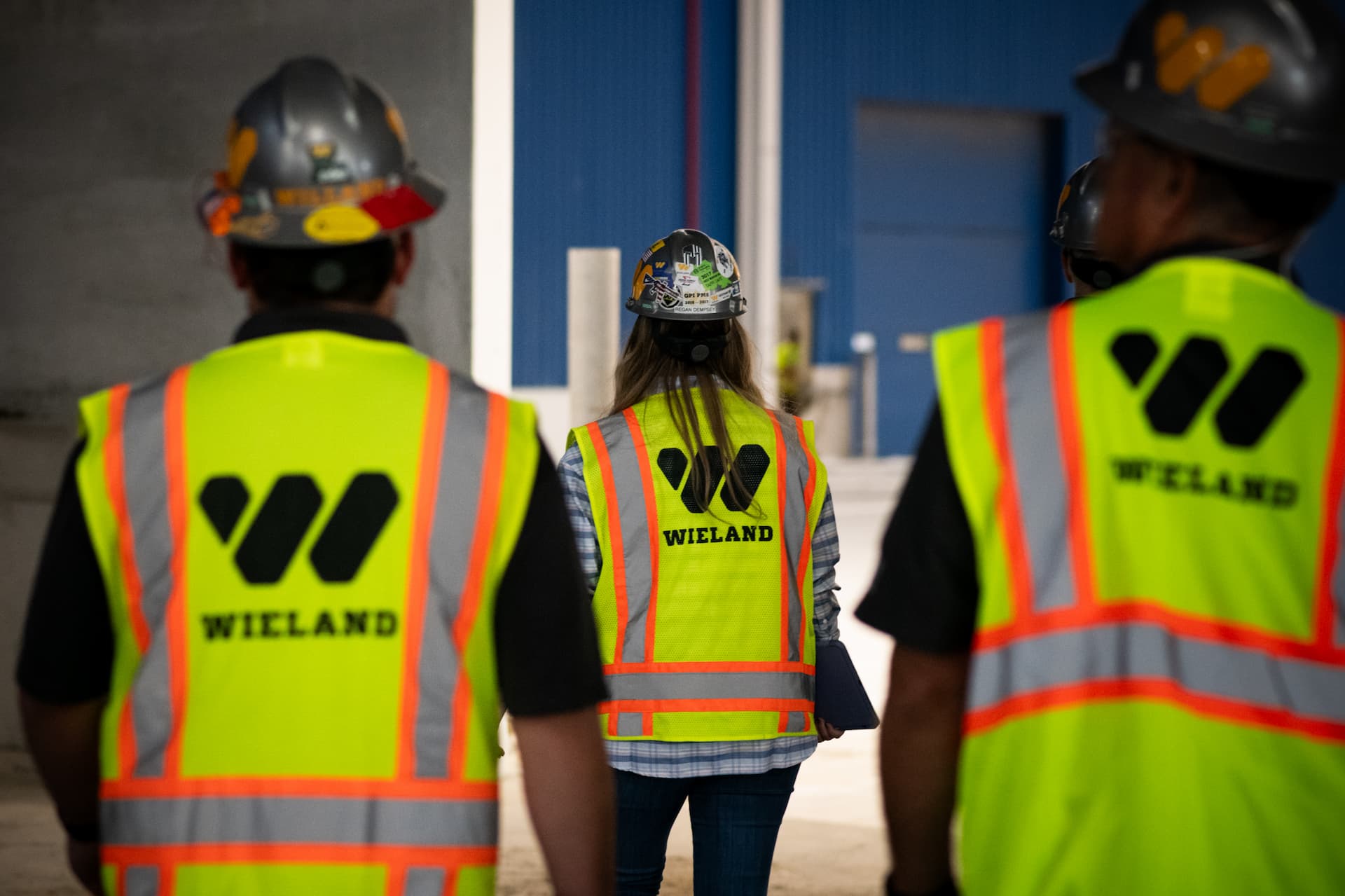 Employees in high vis WIELAND branded vests walk into job site