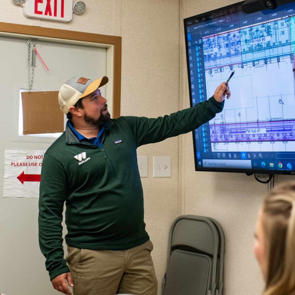 Employee points a blueprint on screen, presenting to team members