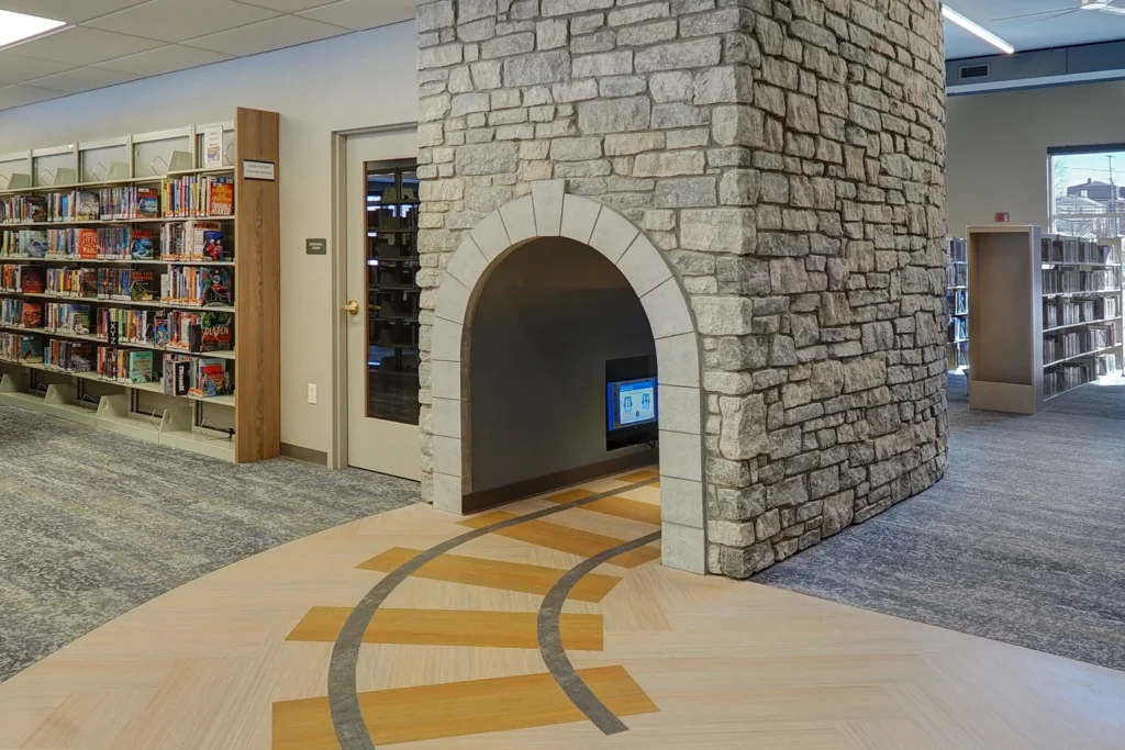 A cozy library featuring a stone fireplace and bookshelves, located at Briggs District Library in St. Johns, MI