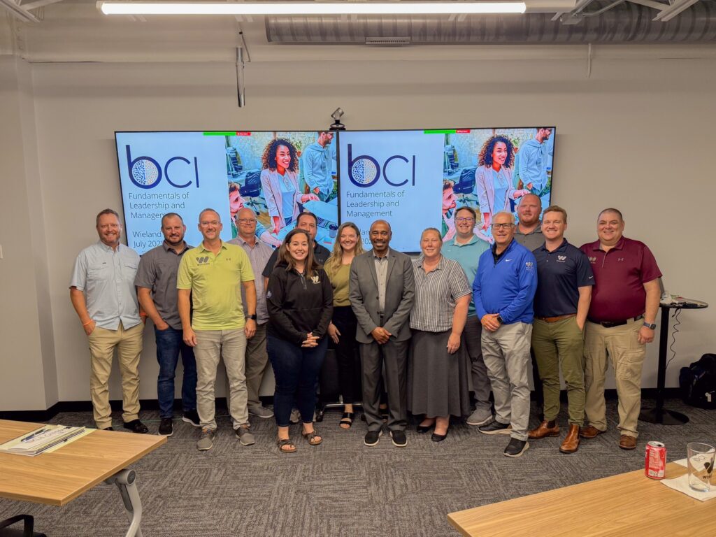 Group of employees posing in front of two tv screens.