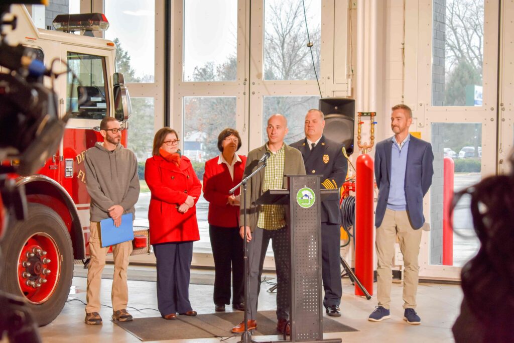 Group gathered around a podium giving speeches about the grand opening of the new fire station.