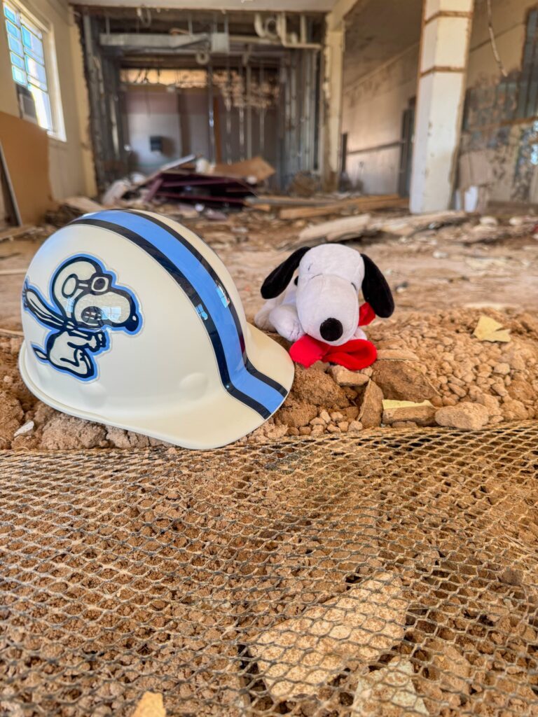 A stuffed animal (Snoopy) on-site during demolition next to a Loyola College Prep hardhat.