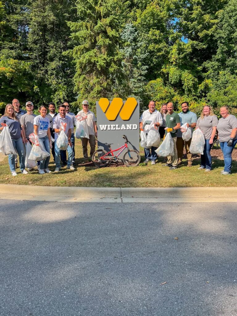 Group standing around the WIELAND sign holding bags of trash collected from Lansing's River Trail.