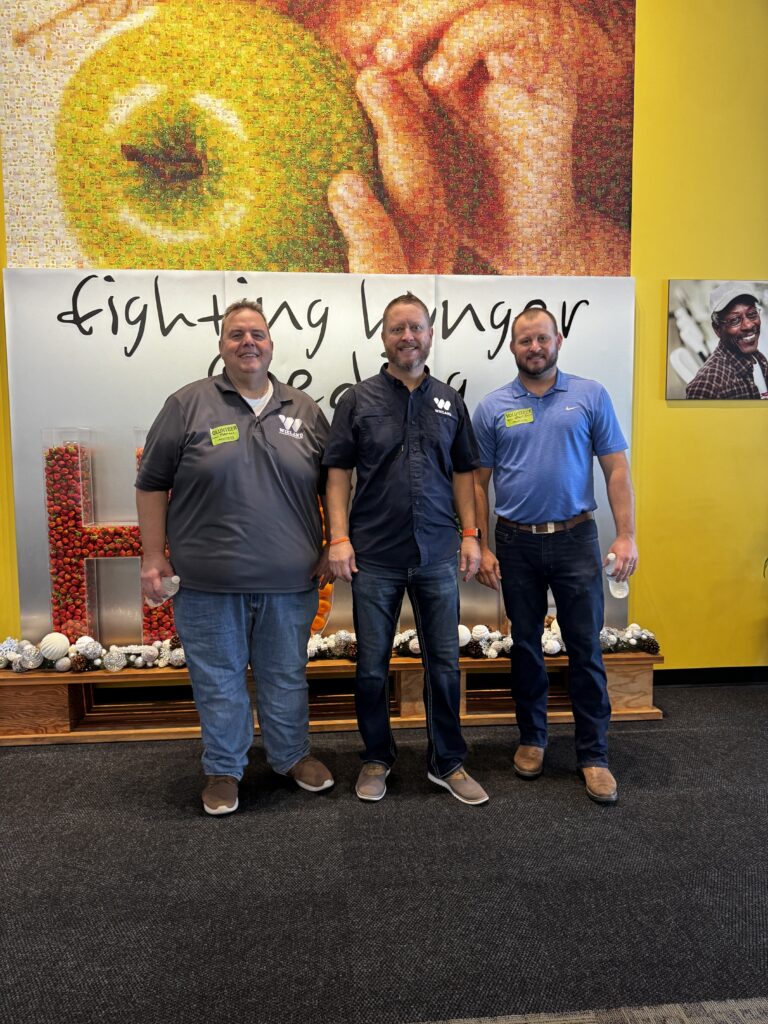 Group of three guys standing by sign that reads "Fighting Hunger one meal at a time".