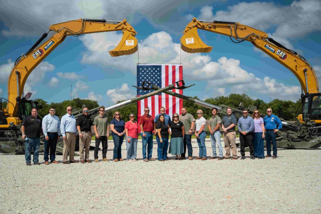 Group gathered under two excavators for a photo while celebrating the Ground Break ceremony